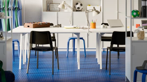 Table blanche, chaises noires et sol bleu avec différents objets et meubles à l’arrière-plan