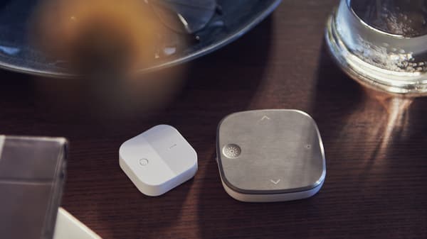 Table brune sur laquelle se trouvent une assiette ronde, un variateur d’intensité sans fil TRÅDFRI blanc et une télécommande STYRBAR en acier inoxydable.