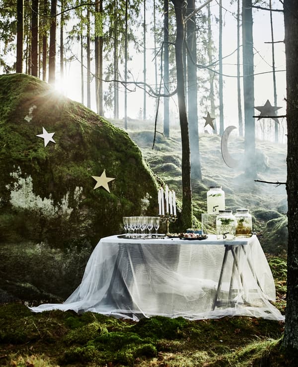 Table de bienvenue avec boissons, garnie d’une nappe en voilage et placée sous une pluie d’étoiles, pour une fête de noces en forêt