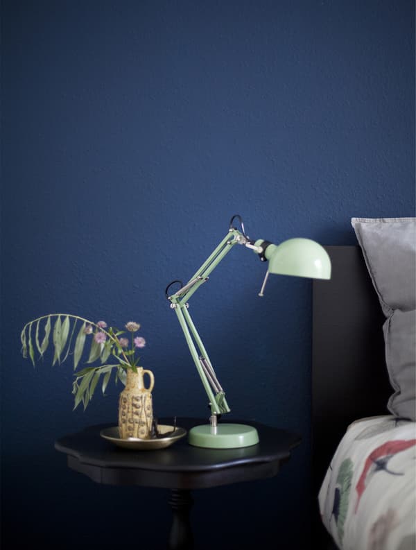 Table de chevet noire avec lampe vert menthe sur fond de mur bleu foncé.