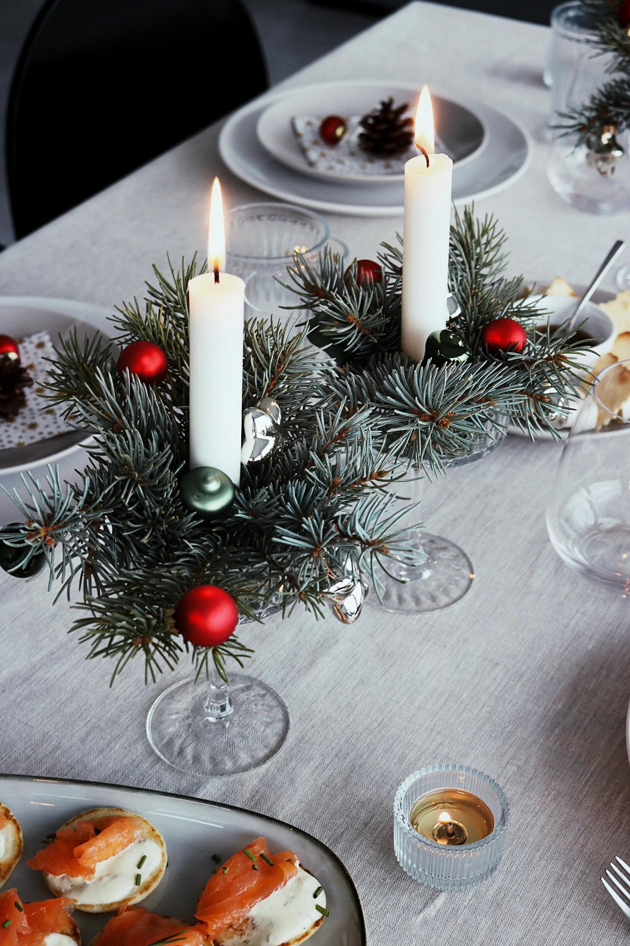 Table de fête décorée de bougies allumées dans des couronnes de verdure, d'ornements rouges et verts et d'assiettes d'amuse-bouches. Ambiance chaleureuse et festive.