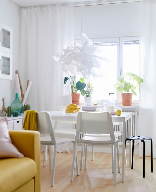 Table de salle à manger et chaises blanches près d’une fenêtre, avec suspension en papier de forme organique au-dessus.