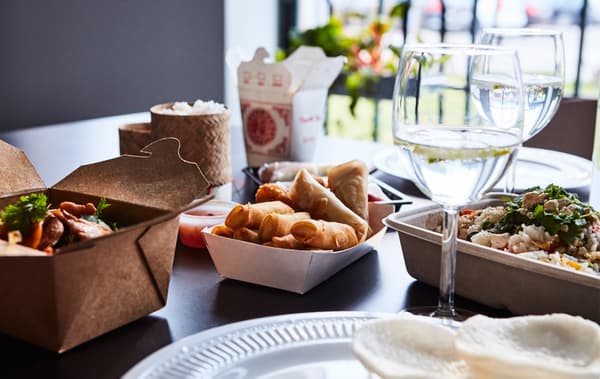 Table dressée avec verres à vin, vaisselle et plats à emporter asiatiques.