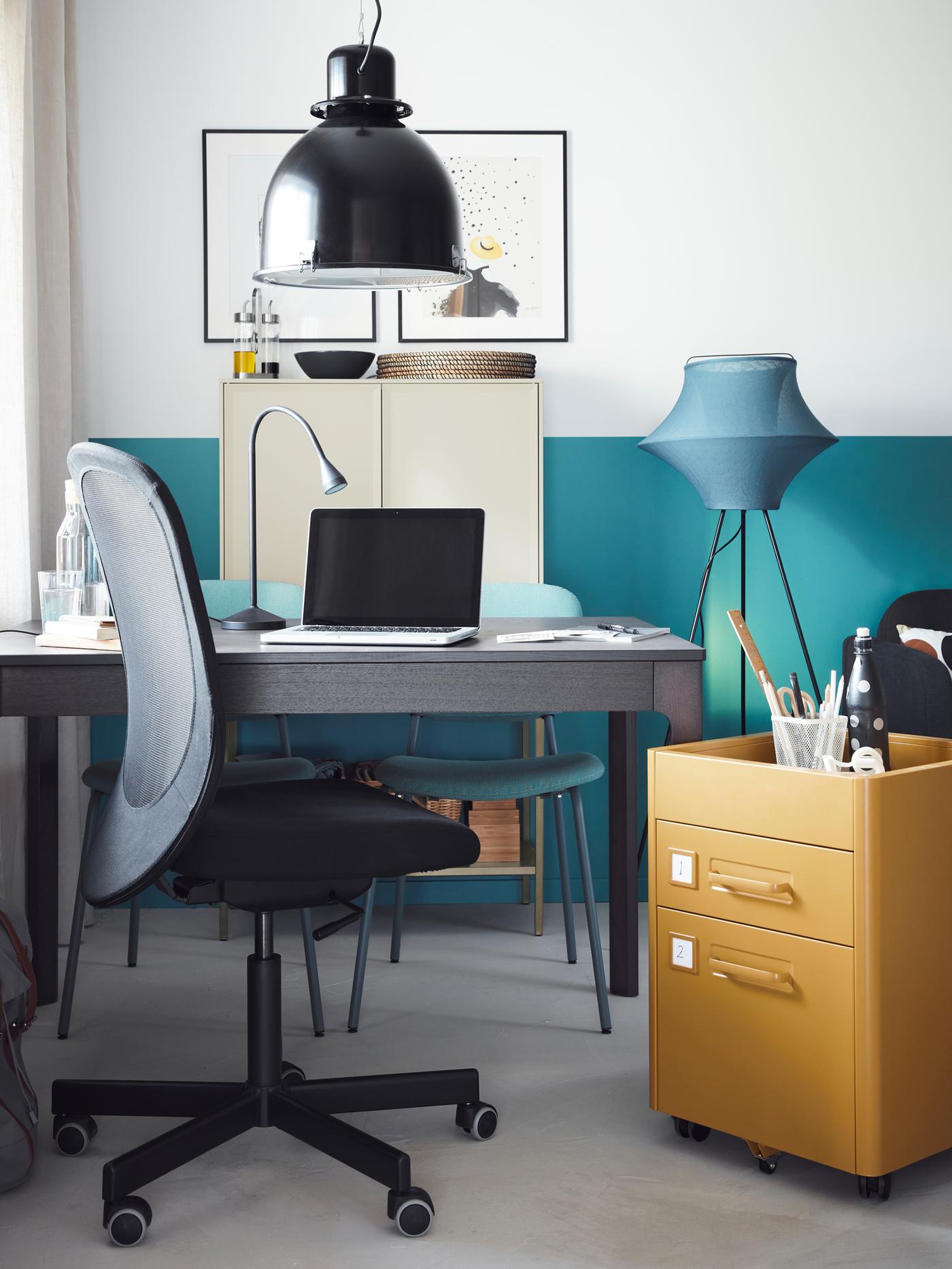 Table EKEDALEN utilisée comme bureau, ordinateur portable sur celle-ci, caisson à tiroirs jaune à côté et chaise pivotante devant.