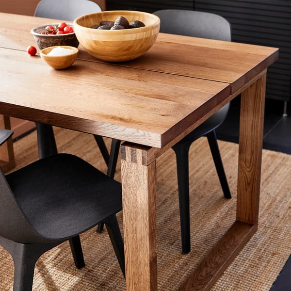 Table en bois marron clair MÖRBYLÅNGA avec variations de couleur et de grains chêne naturel avec chaises modernes foncées assorties.