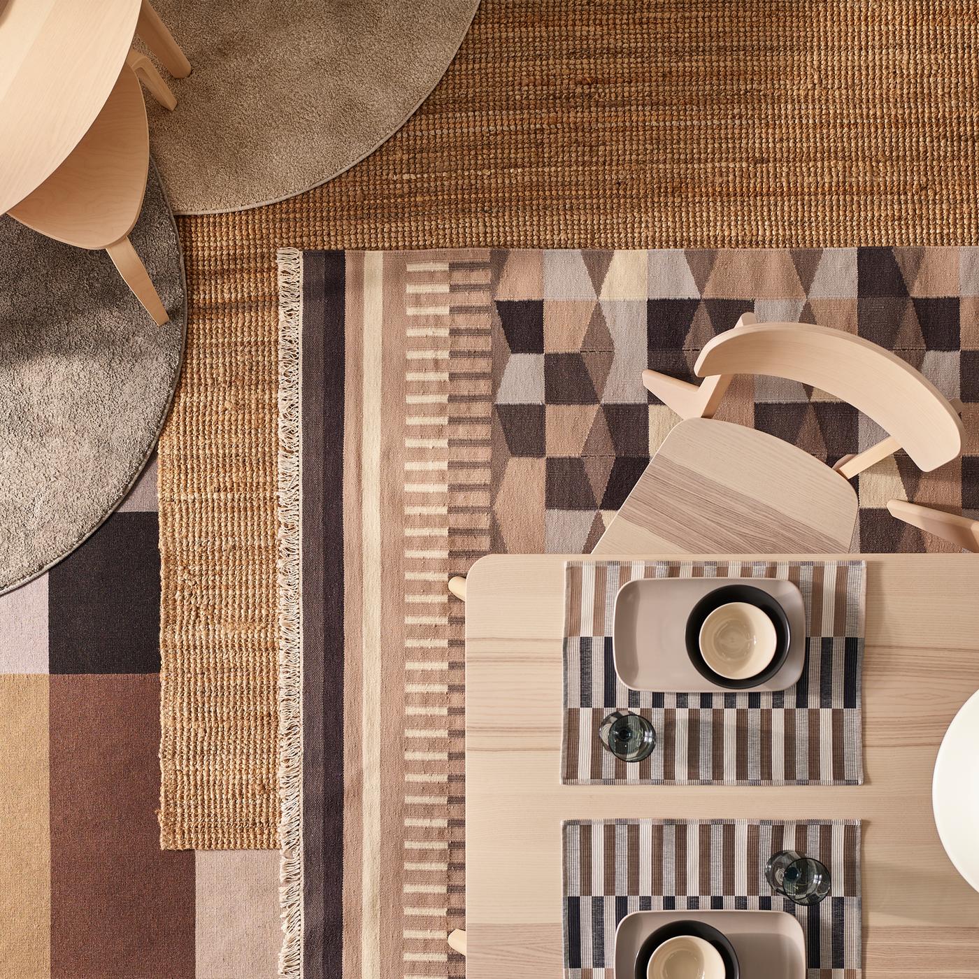 Table et chaise LISABO en plaqué frêne sur plusieurs tapis se chevauchant, dont un tapis LOHALS en fibres naturelles et différents tapis à motifs.