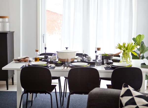 Table et chaises pour six personnes, avec vaisselle monochrome et verdure.