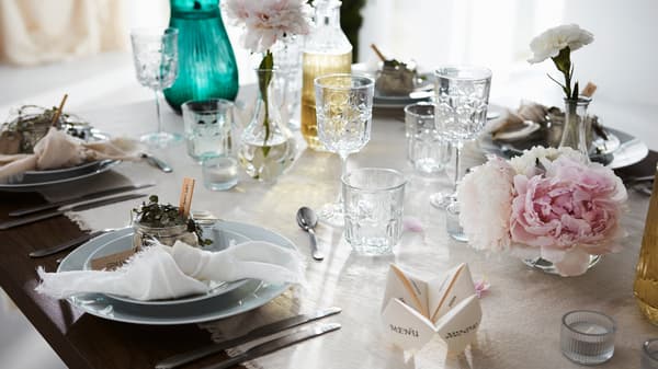 Table festive dressée pour une grande occasion avec nappe de couleur claire, verres délicats, assiettes, couverts et décorations florales.