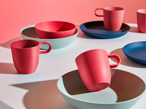 Table ronde dressée avec des assiettes, des bols et des tasses rouges, bleu foncé et vert clair de la série IKEA TALRIK en plastique PLA.