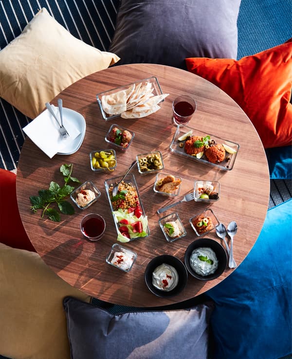 Table ronde sur laquelle sont présentés des mezze dans des bols et des plats, avec coussins posés par terre tout autour.