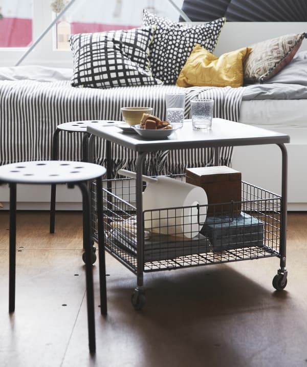 Table sur roulettes avec panier de rangement dans le bas, deux petits tabourets et un divan.