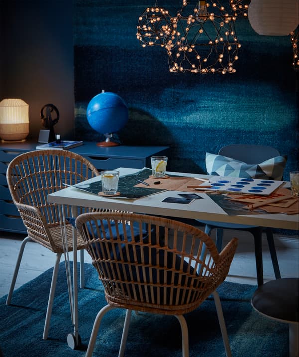 Table with drinks and star maps, wicker-style chairs, LED lighting above and SÖNDERÖD rugs both on the floor and wall.