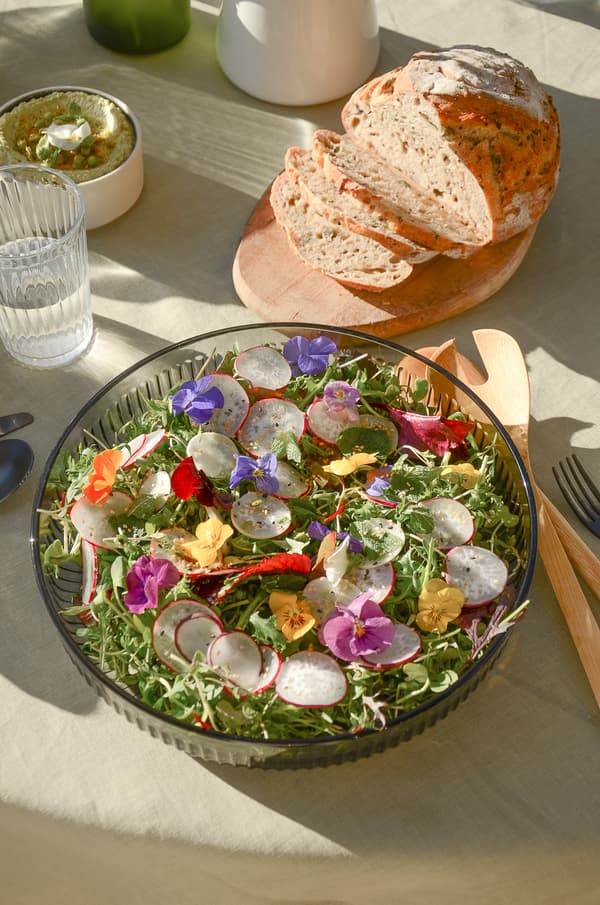Table with salad, bread, water and herb dip, wooden and metal cutlery on light tablecloth.