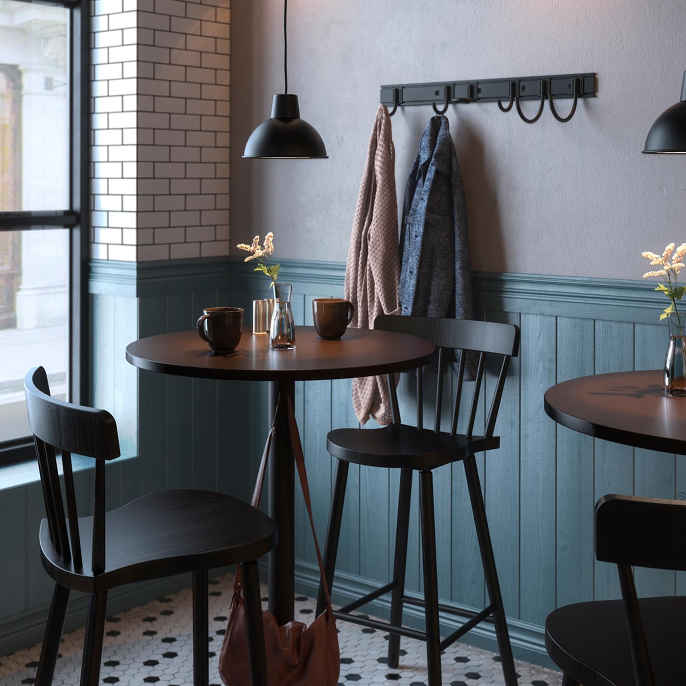 Tables and chairs in a cafe, vases of flowers and diverse items on the tables, lamps and a coat rack on the wall.