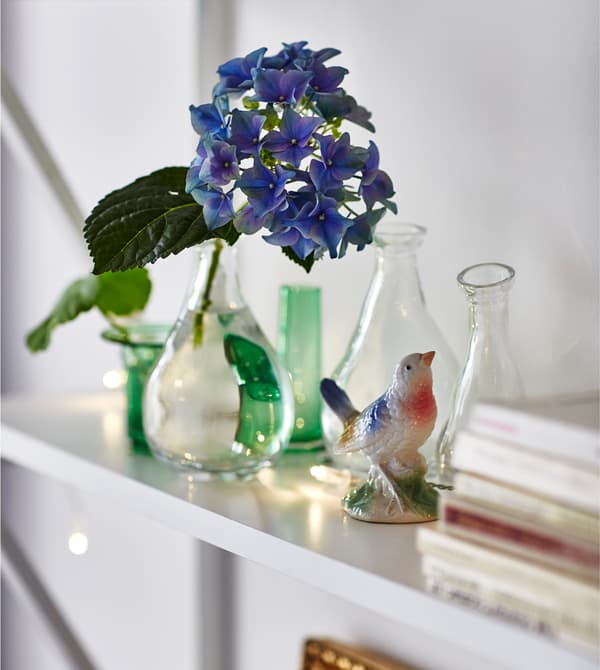 Tablette garnie de petits vases en verre et d’une figurine d’oiseau.