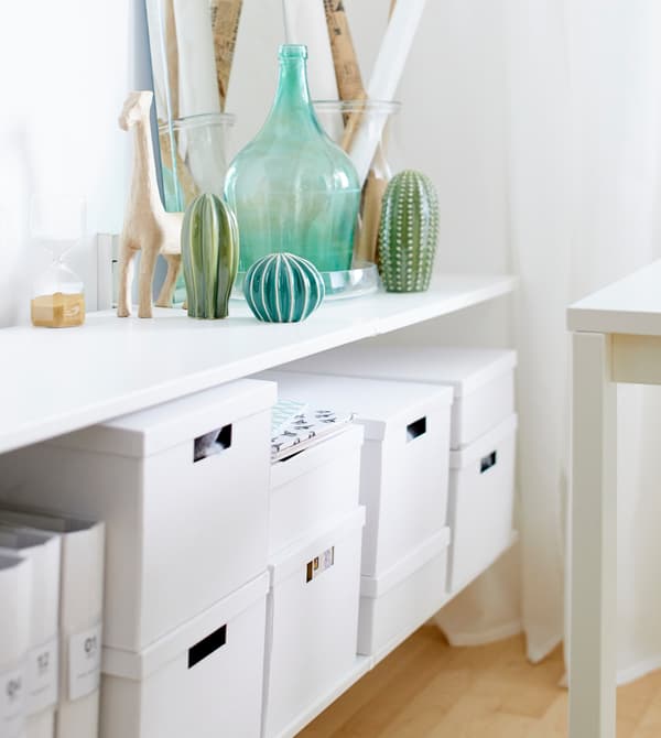 Tablettes blanches décorées de vases verts et d’autres objets et garnies d’une multitude de boîtes de rangement en carton blanches.