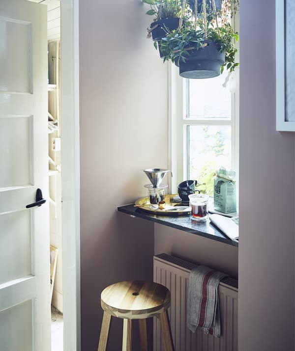 Tabouret et rebord devant une grande fenêtre, avec plantes suspendues et coin pour préparer le café