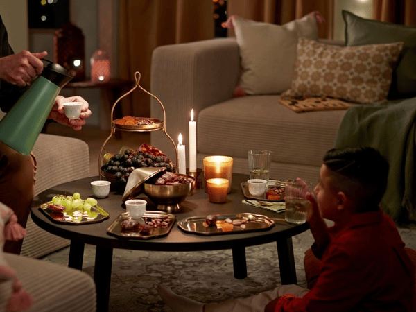  tända ljuslyktor och dukat bord med fat i glänsande mässingstoner och färgglada textilier. 