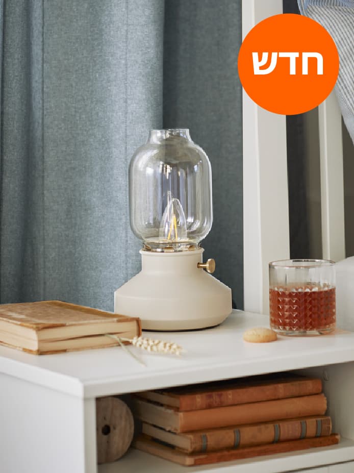 מנורת שולחן TÄRNABY, ספר וכוס עומדים על שידת לילה SONGESAND לבנה ליד מיטת IDANÄS לבנה.