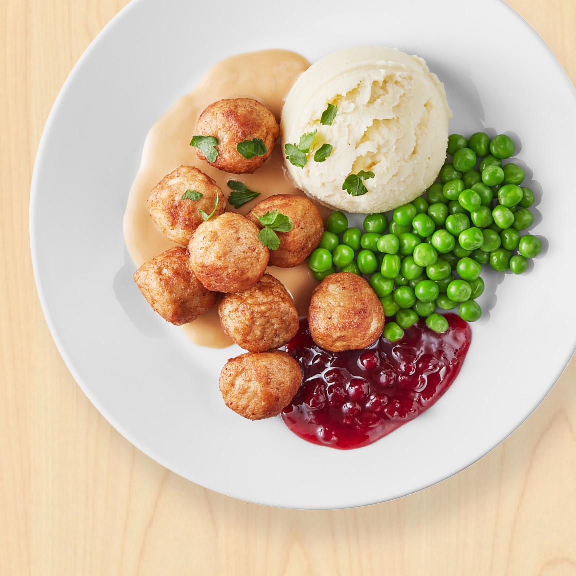 Talíř s masovými kuličkami, bramborovou kaší, hráškem a brusinkami.