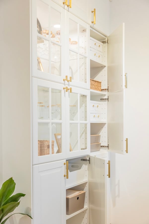 Tall white kitchen cabinet with glass doors and organized storage boxes.