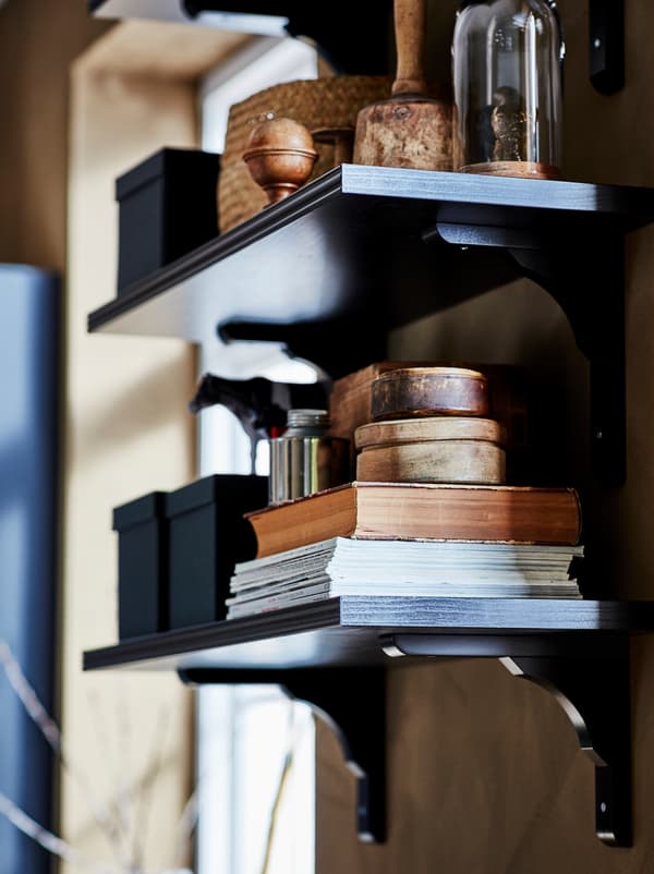 Tamna BERGSHULT/RAMSHULT zidna polica ispunjena časopisima i knjigama, kutijama i rješenjima za izlaganje.