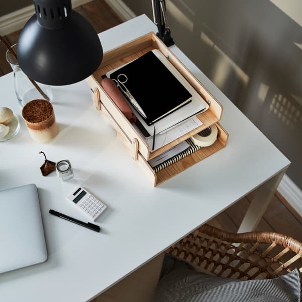 Tampo de mesa com um candeeiro de secretária fixado, um computador portátil e acessórios de escritório, a maioria dos quais está num porta-cartas de madeira com dois andares.