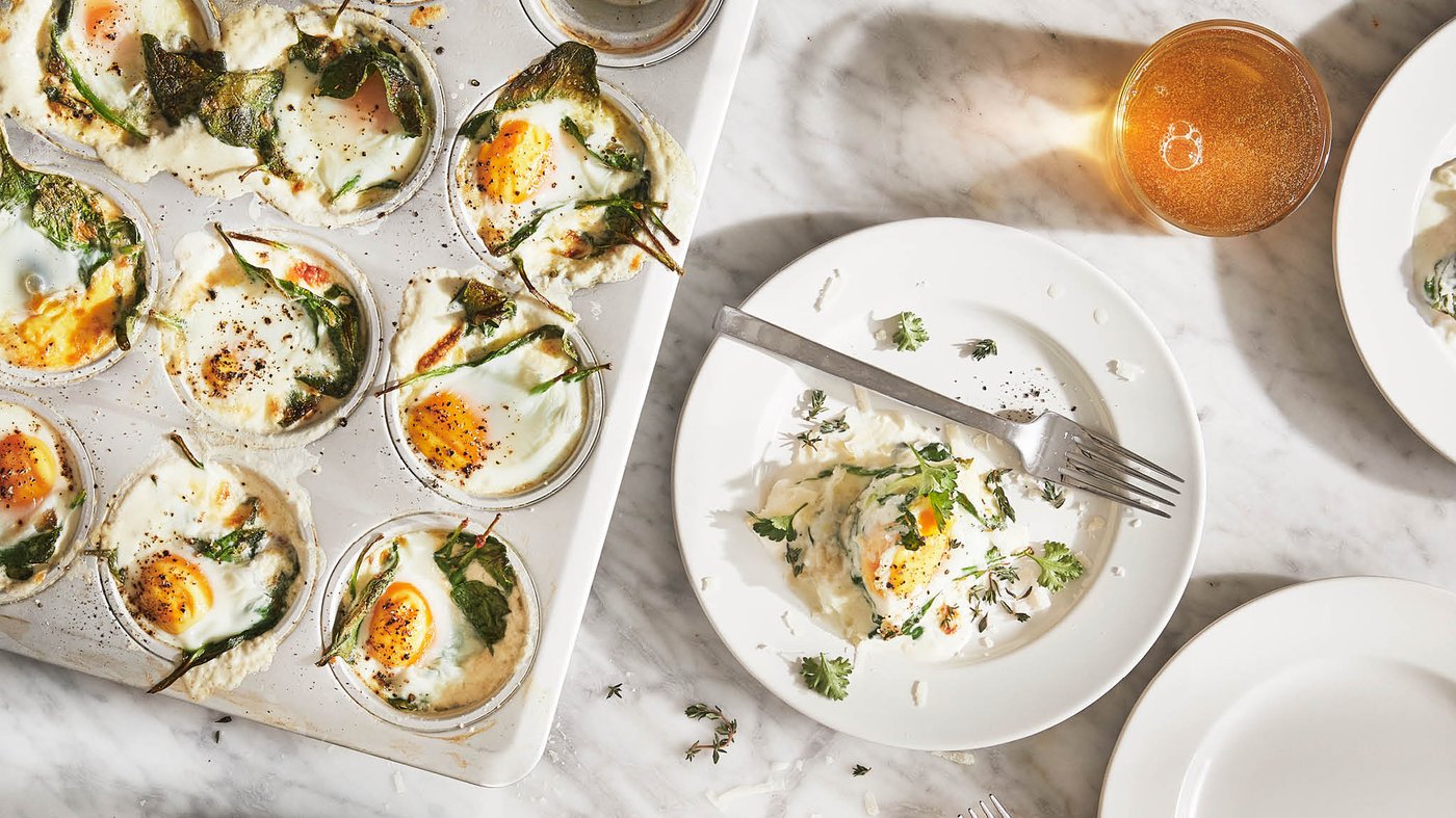 Tanier s jednou porciou zapečených vajec so špenátom a syrom je na stole vedľa formy na mafiny VARDAGEN s ďalšími porciami.