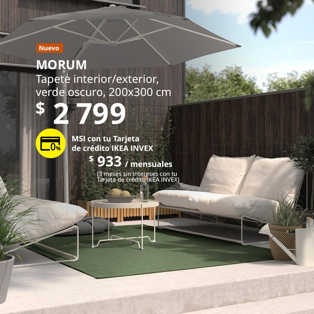 Tapete MORUM para interior y exterior en color verde oscuro, colocado en un área de descanso al aire libre con sofás y sombrilla.