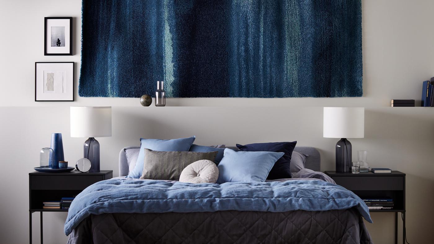 Tapete na parede com mesas de cabeceira VIKHAMMER de cada lado de uma cama de casal SLATTUM em cinzento claro, com roupa de cama KOPPARBLAD.