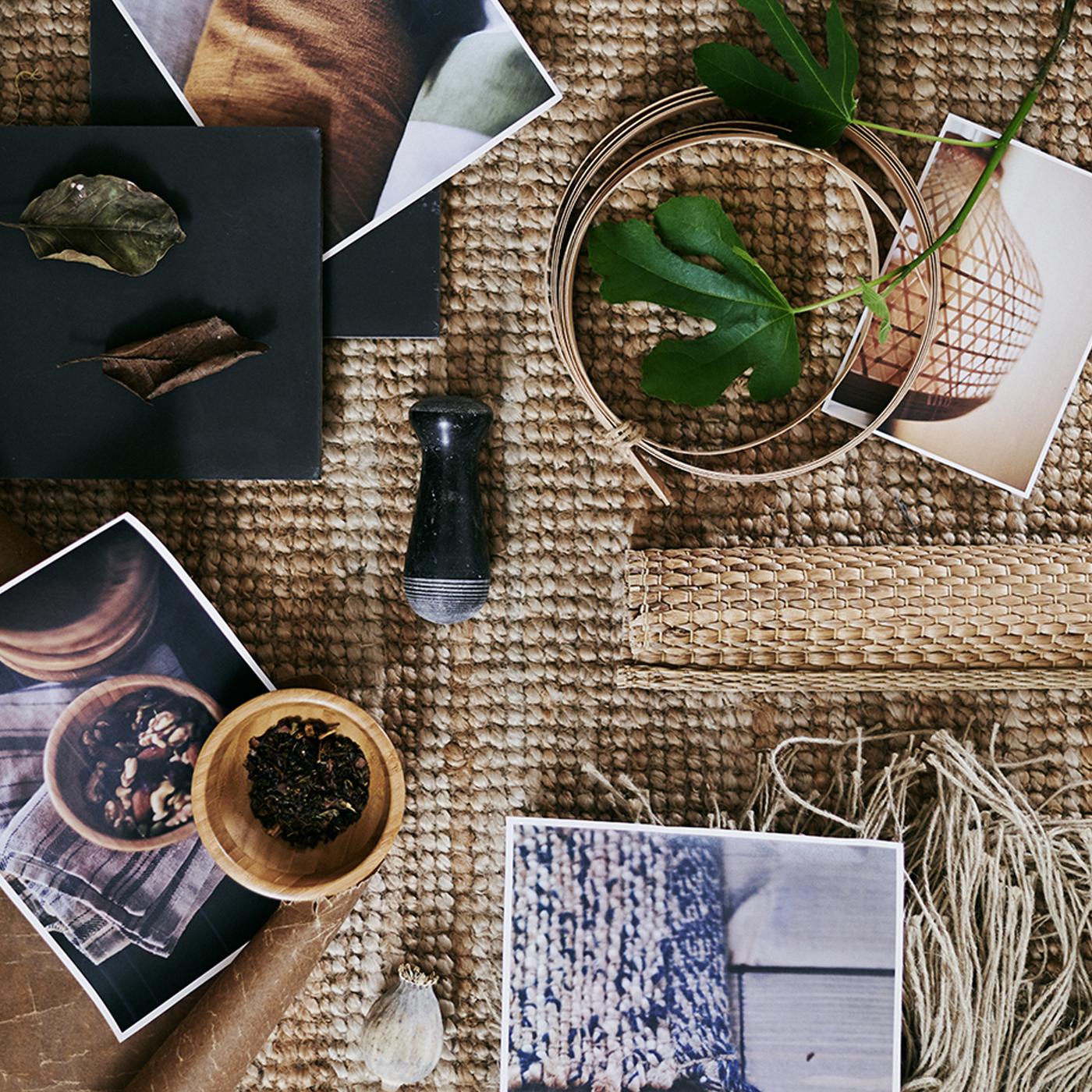 Tapis grossièrement tissé sur lequel sont posées plusieurs photos et différentes matières premières, dont des feuilles et de la laine.