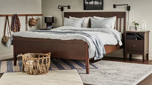 Tapis VRENSTED, VEDBÄK et TVERSTED sous un lit IDANÄS brun foncé habillé de linge de lit BERGPALM bleu/rayé et d’un plaid gris.