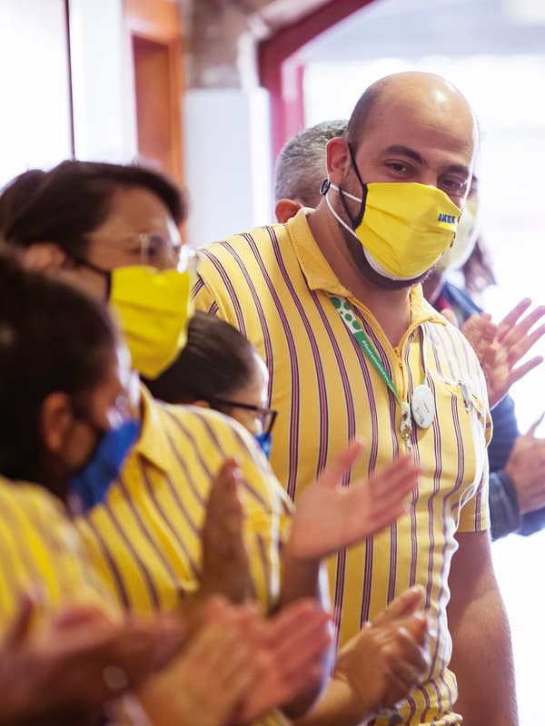 Tarek, a Syrian refugee and IKEA co-worker, smiles down at his colleagues from behind a yellow facemask.
