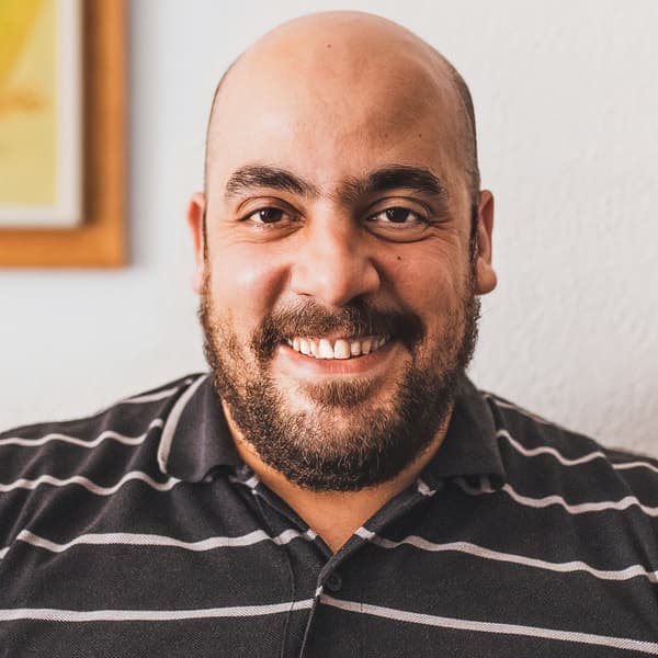 Tarek, a Syrian refugee and IKEA Spain co-worker, smiles while wearing a brown and white striped shirt.