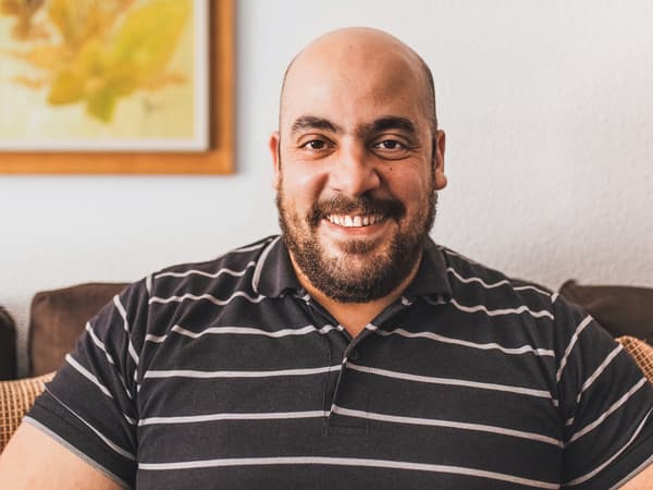 Tarek, en syriansk flykting och medarbetare på IKEA Spanien, som ler och har en brun-vitrandig skjorta på sig.