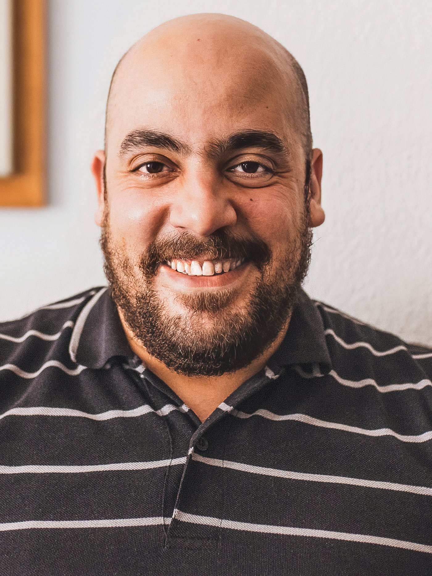 Tarek, un refugiat sirià i col·laborador d’IKEA a Espanya, somrient amb una camisa de ratlles marró i blanca.