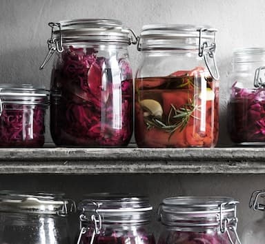 Tarros de vidrio en un estante llenos con col en vinagre y pimientos rojos.