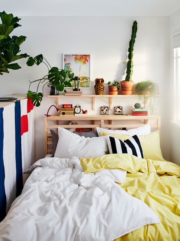 เตียง TARVA/ทาร์ฟวา และเครื่องนอน ÄNGSLILJA/เอ็งส์ลิลยา สีเหลืองกับสีขาว ต้นไม้และของตกแต่งอยู่บนชั้นวางเหนือเตียง