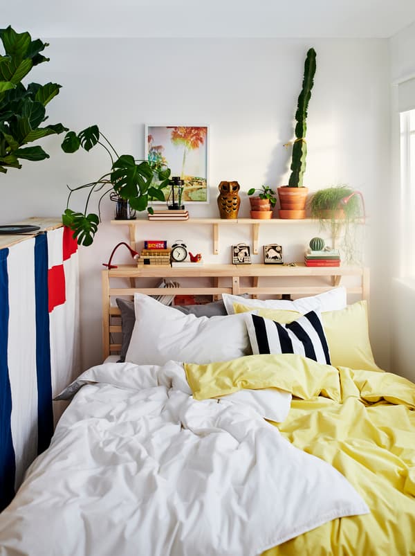 TARVA bed with two sets of ÄNGSLILJA bed linen, one yellow and one white. Plants and decorations on a shelf above the bed.