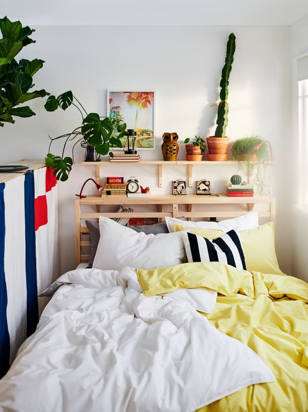 TARVA bed with two sets of ÄNGSLILJA bed linen, one yellow and one white. Plants and decorations on a shelf above the bed.