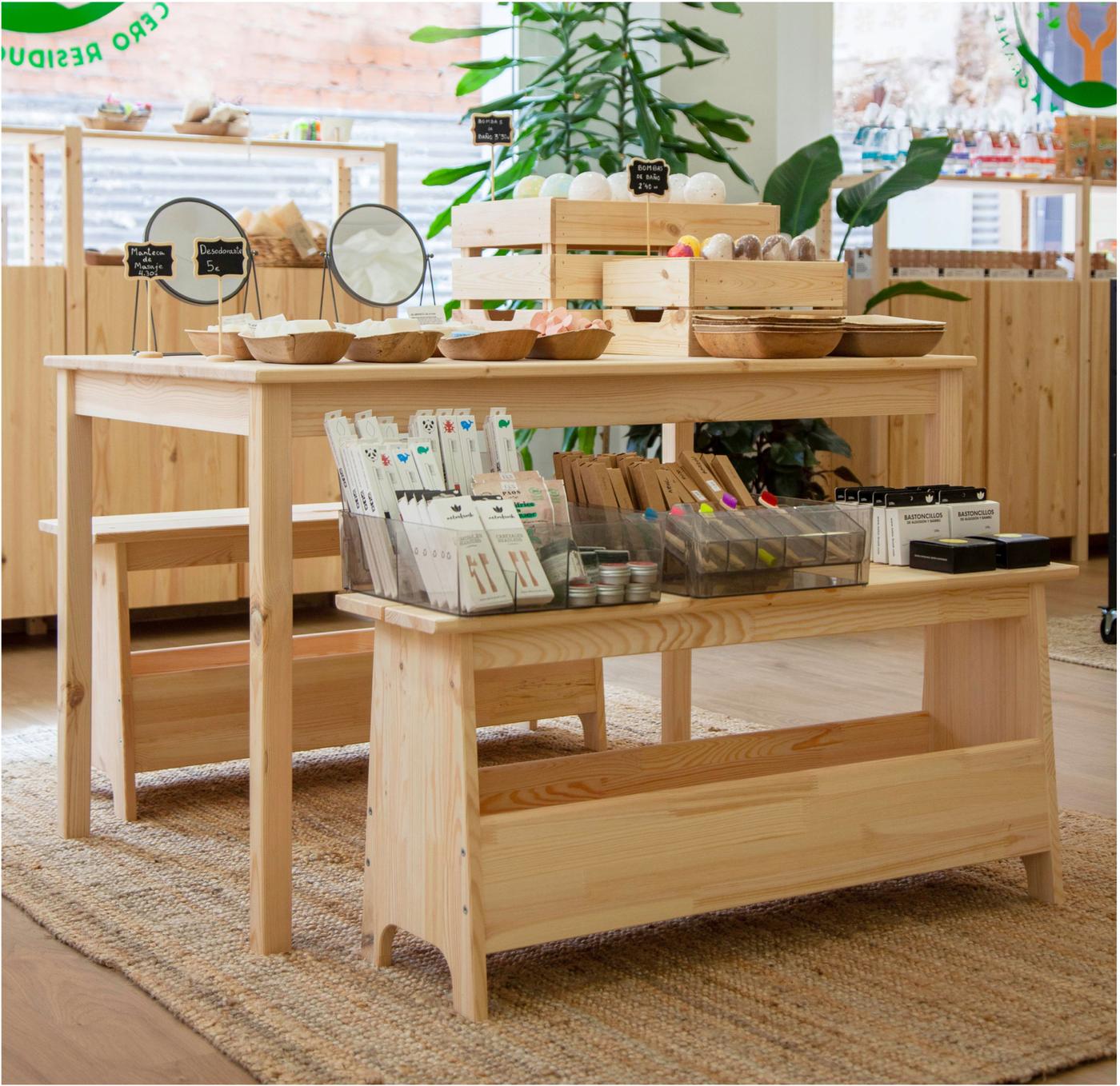 Taules de fusta amb productes sostenibles en contenidors de fusta i paper, disposats en un espai de botiga lluminós.