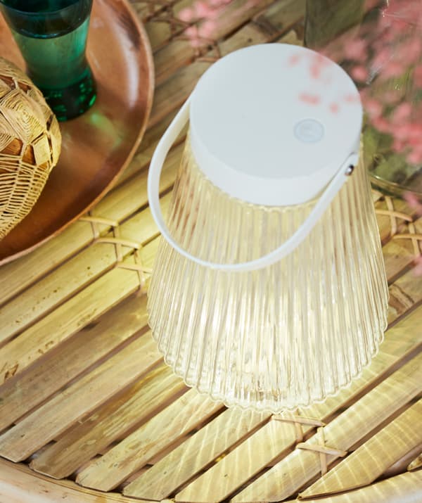 Tavolo con sottili stecche in legno, con sopra un vassoio e una lampada LED a energia solare SOLVINDEN, che emana una luce soffusa - IKEA