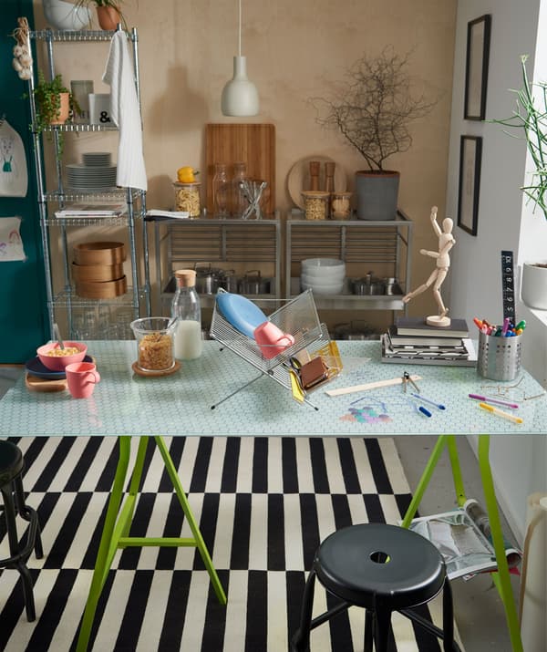 Tavolo da pranzo in vetro utilizzato per metà per mangiare e per metà per attività creative, con uno scolapiatti usato come divisorio.