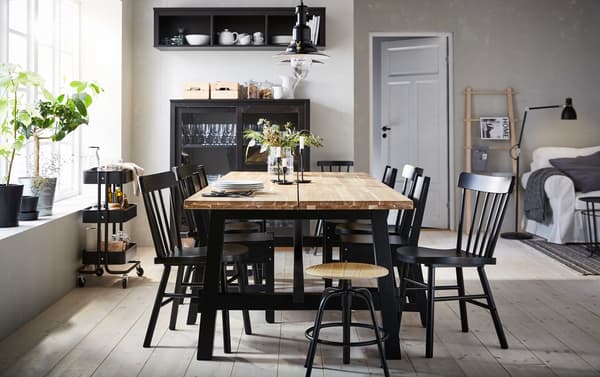 Tavolo SKOGSTA in acacia al centro di una zona pranzo beige e nera, circondato da sedie nere di diverso tipo – IKEA