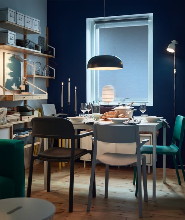 Tavolo VANGSTA con sedie JANINGE colorate. L'ambiente è illuminato da una lampada in acciaio nero NYMÅNE a sospensione e una lampada in carta STORUMAN bianca.