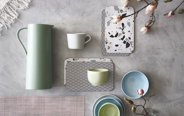 Tazze e vassoi in colori pastello disposti su un ripiano in cemento - IKEA