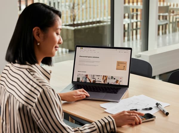 テーブルでノートPCを操作する人。IKEA for Businessのインテリアプランニングサービスのページを見ながら資料を確認している。