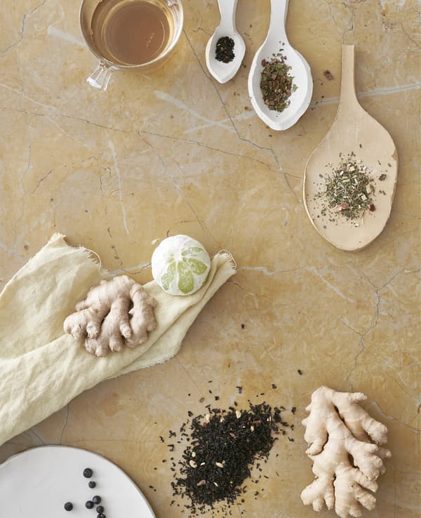 Tea leaves in ceramic spoons, ginger root and a lime.