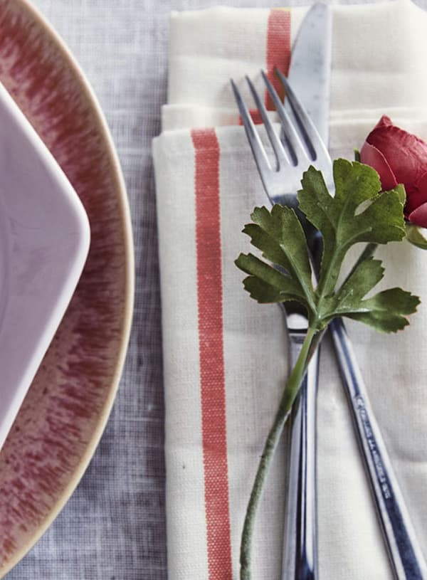 Tea towel folded with utensils and artificial rose placed on top