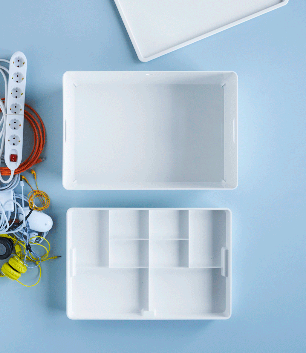 Tech accessories and chargers waiting to be put away in a white IKEA KUGGIS box with two levels.